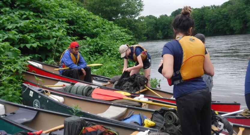 A group of people stand in ankle deep water around three canoes